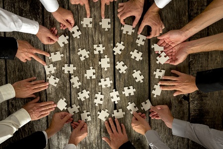 High Angle View of Businessmen Hands Forming Circle and Holding Puzzle Pieces on Top of a Rustic Wooden Table.